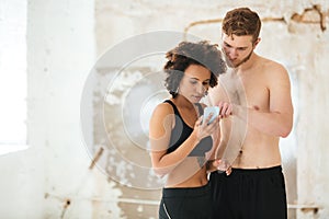 Multicultural young sport couple using mobile phone while standing