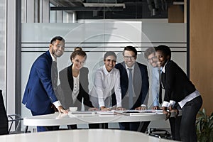 Multiethnic ambitious employees gather in boardroom smile staring at camera