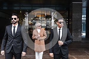 multiethnic bodyguards in sunglasses escorting mature