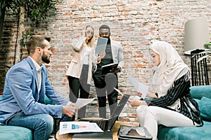 Multiethnic business people on the meeting. Muslim woman and Caucasian man reading project reports sitting on the sofas