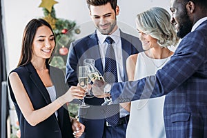 multiethnic businesspeople clinking with glasses of champagne with christmas tree on background