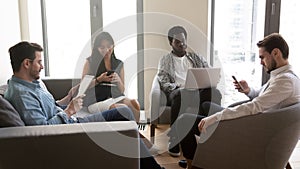 Multiethnic businesspeople rest in office lobby chatting using diverse gadgets