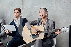 Multiethnic businesswomen playing guitar and using digital tablet