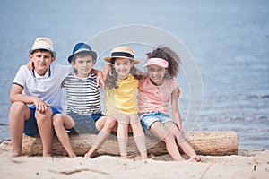 multiethnic children hugging each other while sitting on wooden trunk