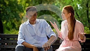 Multiethnic couple arguing sitting on bench in park, jealousy, misunderstanding