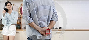 Multiethnic couple having romantic dinner in home kitchen. A man stands with a box with a wedding ring behind him