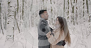 Multiethnic couple hugging each other in winter forest