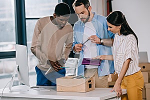 multiethnic coworkers unpacking box with office supplies