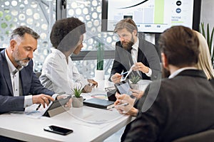 Multiethnic diverse business colleagues at meeting in office room with plasma screen. Handsome young bearded team boss