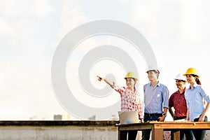 Multiethnic diverse group of engineers or business partners at construction site, pointing toward copy space on sky during sunset