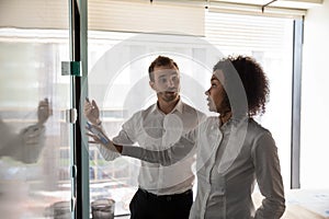 Multiethnic employees draw on glass door cooperating in office