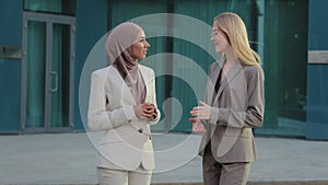 Multiethnic female colleagues discussing report outside. Happy businesswomen in office suits and hijab standing outdoors