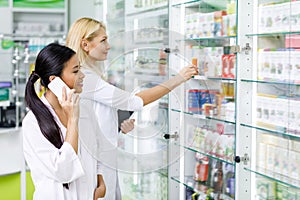 multiethnic female pharmacists using digital devices while working