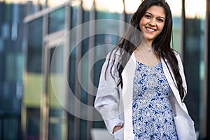 Multiethnic female professional doctor in a white coat standing out side of private practice, possibly physician, dental hygienist