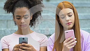 Multiethnic female teens chatting on smartphones, real communication lack