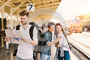 Multiethnic group of backpack travelers using map and smartphone navigation at train station, Asian tourism activity concept