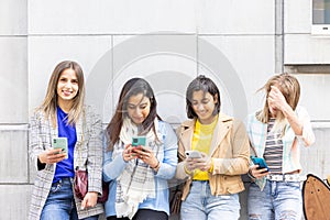Multiethnic Group of beautiful young female friends standing against a wall using mobile smartphones