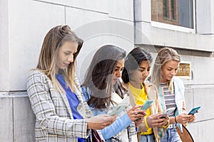 Multiethnic Group of beautiful young female friends standing against a wall using mobile smartphones