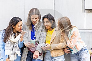Multiethnic Group of beautiful young female friends standing against a wall using mobile smartphones