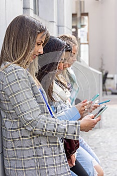 Multiethnic Group of beautiful young female friends standing against a wall using mobile smartphones