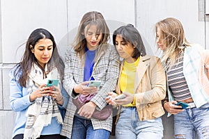 Multiethnic Group of beautiful young female friends standing against a wall using mobile smartphones