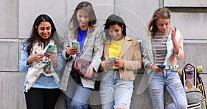 Multiethnic Group of beautiful young female friends standing against a wall using mobile smartphones