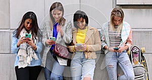 Multiethnic Group of beautiful young female friends standing against a wall using mobile smartphones