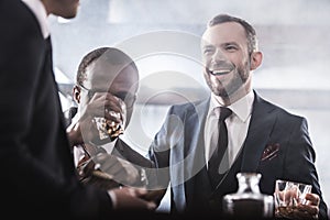 Multiethnic group of businessmen spending time together drinking whiskey and smoking