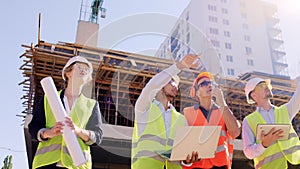 Multiethnic group of diverse specialists and middle -aged foreman walking down the construction site using digital