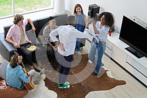 Multiethnic group of friends having fun at home. Young people dancing, playing guita and drinking wine in living room