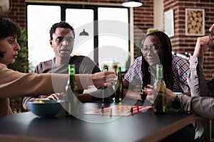 Multiethnic group of friends sitting at table while playing boardgames with figurines.