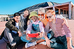 Multiethnic group of friends taking pictures together sitting outdoors under blue sky.