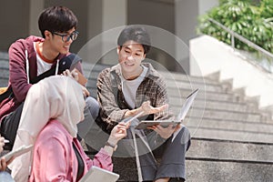 A multiethnic group of university students is studying together while sitting on steps near the campus and communicating