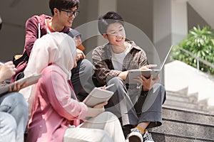 A multiethnic group of university students is studying together while sitting on steps near the campus and communicating