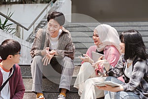 A multiethnic group of university students is studying together while sitting on steps near the campus and communicating