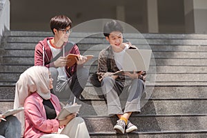 A multiethnic group of university students is studying together while sitting on steps near the campus and communicating