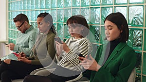Multiethnic group of young diverse ethnicity candidates using smartphones while waiting job interview in modern office