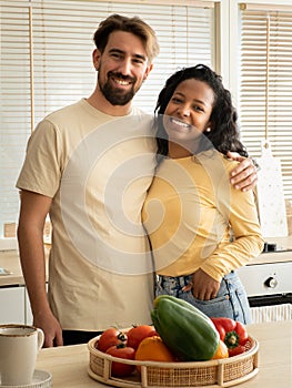 Multiethnic heterosexual couple smiling in the kitchen of an apartment.