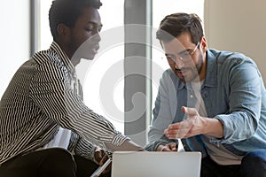 Multiethnic male colleagues discuss business project on laptop