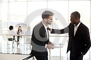 Multiethnic male employees standing in hallway laughing at joke