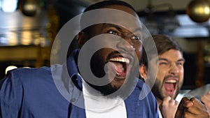 Multiethnic men cheering for sports team winning match, celebrating goal in pub