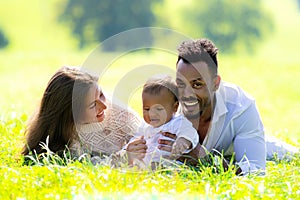 Multiethnic parents and mixed race baby in park. Multiethnic family outdoor portrait. Biracial baby child on yard