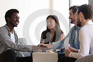 Multiethnic partners sitting on couch shake hands start group meeting