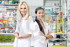 multiethnic pharmacists in white coats standing with crossed arms and smiling at camera