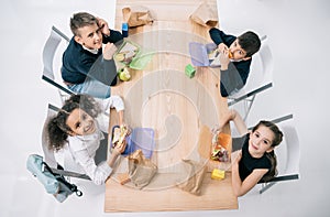 Multiethnic schoolkids eating lunch while sitting at table and smiling at camera