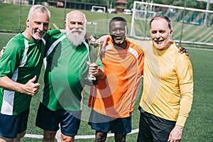 multiethnic smiling old sportsmen with champions cup standing