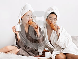 Multiethnic spa girlfriends enjoying breakfast, sitting on bed