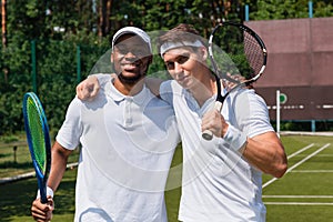 Multiethnic sportsmen with tennis rackets hugging