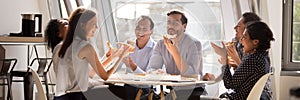 Multiethnic staff gathered together in office kitchen laughing eating pizza