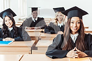 group of multiethnic students in graduation costumes sitting